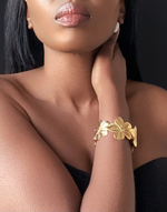 Cargar imagen en el visor de la galería, Close-up of a model wearing the ABYDOS Flower Cuff Bracelet, featuring a bold floral design in 18k gold-plated stainless steel, elegantly styled for a sophisticated look.
